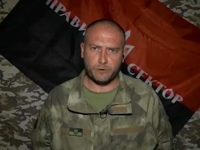 Este es Dimitro Yarosh. Detrás de él puede verse la bandera negra y roja, ‎con el Tridente ucraniano, que enarbolaba el “nacionalista” Stepan Bandera. Dimitro Yarosh es ‎un agente de las redes secretas “stay-behind” de la OTAN. En 2007, Yarosh estableció una ‎alianza entre los neonazis europeos y los yihadistas del Medio Oriente para que todos lucharan ‎juntos contra Rusia. Dimitro Yarosh tuvo un papel central en la operación de “cambio de ‎régimen” realizada en Ucrania en 2014. El presidente Zelenski, lo nombró consejero especial ‎del jefe de las fuerzas armadas, cargo que ocupa actualmente.