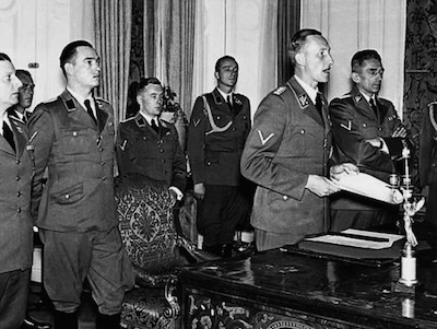 A la derecha, Reinhard Heydrich pronuncia un discurso en el Castillo de Praga. Oficialmente nombrado Protector Adjunto de Bohemia y Moravia, Heydrich en realidad se ocupaba de coordinar la aplicación de la “Solución Final” contra los judíos y los gitanos. En 1942, el ucraniano Dimitro Dontsov se incorporó al equipo del SS Heydrich y supervisó masacres en toda Europa hasta la caída final del III Reich. Hoy la historia se repite ya que el Castillo de Praga acogió en octubre la reunión de la Comunidad Política Europea contra la Federación Rusa.
