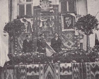 Celebración de la Ucrania “independiente” en presencia de dignatarios ‎nazis. Detrás de los oradores se ven los retratos –de izquierda a derecha– de Stepan Bandera, ‎Adolf Hitler y Yevhen Konovalets.‎